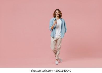 Full Length Young Happy Man With Long Curly Hair Wear Blue Shirt White T-shirt Hold Takeaway Delivery Craft Paper Brown Cup Coffee To Go Isolated On Pastel Plain Pink Color Wall Background Studio.