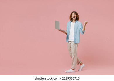 Full Length Young Happy Man With Long Curly Hair Wear Blue Shirt White T-shirt Hold Use Work On Laptop Pc Computer Do Winner Gesture Isolated On Pastel Plain Pink Color Wall Background Studio Portrait