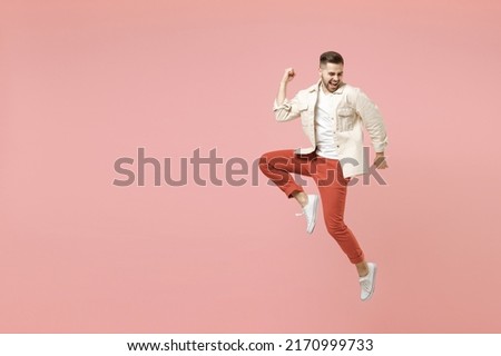Full length young happy overjoyed fun trendy fashionable caucasian man 20s in jacket white t-shirt jump do winner gesture clench fist celebrating isolated on pastel pink background studio portrait.