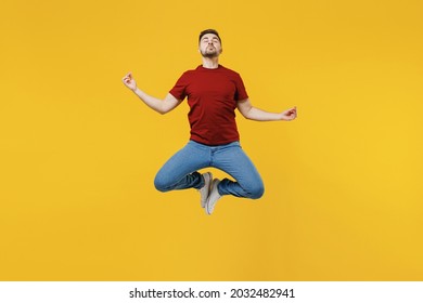 Full Length Young Man 20s In Red T-shirt Jump High Hold Spread Hand In Yoga Om Aum Gesture Relax Meditate Try Calm Down Isolated On Plain Yellow Color Wall Background Studio. People Lifestyle Concept