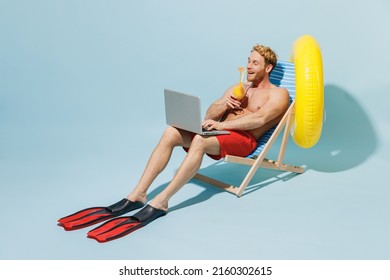 Full length young man 20s in red shorts swimsuit sit in deckchair inflatable ring hold cocktail use laprop pc computer work isolated on pastel blue background Summer vacation sea rest sun tan concept.