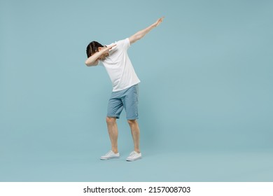 Full length young man in white casual basic t-shirt doing dab hip hop dance hands move gesture youth sign hide cover face isolated on pastel blue background studio portrait People lifestyle concept.