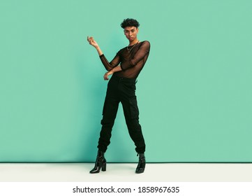 Full Length Of A Young Man With Womens Clothing Posing At Studio With Expression. Gay Man Wearing Black Mesh T-shirt, Jeans And High Heels Looking At Camera.