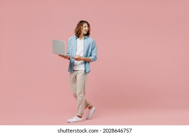 Full length young minded happy man with long curly hair wear blue shirt white t-shirt hold use work on laptop pc computer look aside isolated on pastel plain pink color wall background studio portrait - Powered by Shutterstock