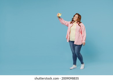 Full Length Young Redhead Chubby Overweight Woman 30s With Curly Hair Wear Pink Shirt Casual Clothes Doing Selfie Shot On Mobile Phone Post Photo On Social Network Isolated On Pastel Blue Background