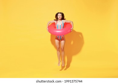 Full length young sexy woman slim body wear red blue swimsuit jump into water hold inflatable rubber ring isolated on vivid yellow color background studio. Summer hotel pool sea rest sun tan concept