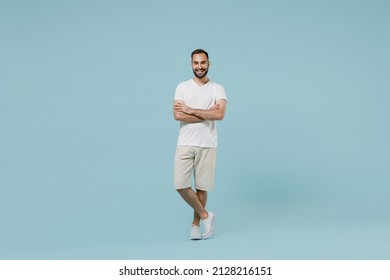 Full length young smiling friendly cheerful happy man 20s wearing casual white t-shirt looking camera hold hands crossed folded isolated on plain pastel light blue color background studio portrait.