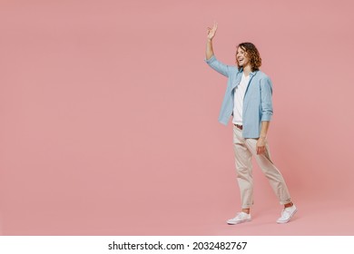 Full Length Young Smiling Happy Stylish Friendly Man 20s With Long Curly Hair In Blue Shirt White T-shirt Walking Going Waving Hand Isolated On Pastel Plain Pink Color Wall Background Studio Portrait