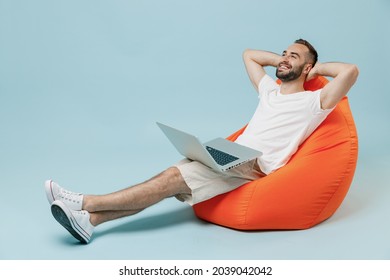 Full length young smiling happy man 20s in white t-shirt sit in bag chair hold use work on laptop pc computer hold hands behind neck rest relax isolated on plain pastel light blue background studio. - Shutterstock ID 2039042042