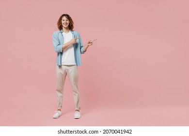 Full Length Young Smiling Happy Man 20s With Long Curly Hair In Blue Shirt White T-shirt Walk Point Index Finger Aside On Workspace Area Mock Up Isolated On Pastel Plain Pink Color Background Studio