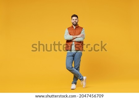 Full length young smiling happy confident smiling cheerful fun caucasian man 20s years old wearing orange vest mint sweatshirt hold hands crossed folded isolated on yellow background studio portrait.