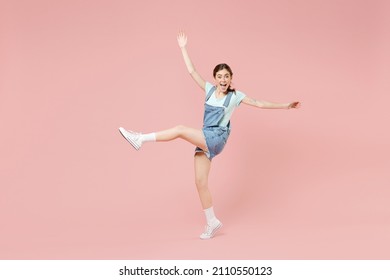 Full Length Young Smiling Joyful Caucasian Woman 20s In Trendy Denim Clothes Blue T-shirt Stand On Toes Dancing With Outstretched Hands Raised Up Leg Isolated On Pastel Pink Background Studio Portrait