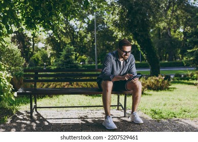 Full length young smiling man 20s in blue shirt glasses sit on bench using mobile cell phone chat rest relax in spring green city park sunshine lawn outdoors on nature Urban lifestyle leisure concept - Powered by Shutterstock