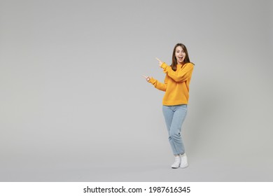 Full length of young smiling positive caucasian happy woman 20s in knitted yellow sweater stand point index finger aside on workspace copy space area isolated on grey color background studio portrait. - Shutterstock ID 1987616345