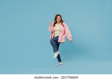 Full Length Young Smiling Redhead Chubby Overweight Woman 30s With Curly Hair Wear In Pink Shirt Jeans Casual Clothes Do Winner Gesture Clench Fist Isolated On Pastel Blue Background Studio Portrait.