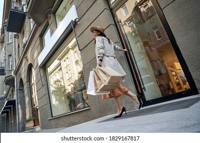 Full Length Of A Young Stylish Woman With Shopping Bags Entering Fashion Boutique Or Shop In City And Smiling