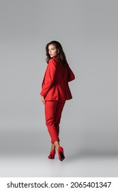 Full Length Of Young Stylish Woman In Red Heels And Suit Posing While Walking On Grey