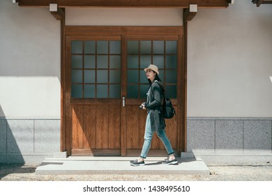 full length young travel woman backpacker walking down streets of old town in osaka. vintage photo of girl tourist passing by old japanese wood building. female visitor carrying camera relax by sun. - Powered by Shutterstock