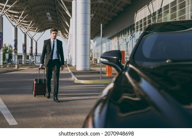 Full length young traveler businessman young man 20s wear black dinner suit going walk outside at international airport terminal with suitcase to car booking taxi. Air flight business trip concept.