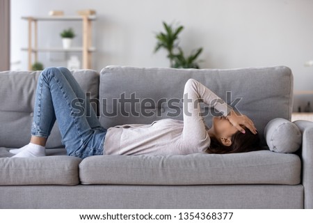 Full length young woman lying on sofa suffers from heartache cover face with hands crying feels desperate unhappy unwell having mental pain or serious health problems, beak up divorce abortion concept