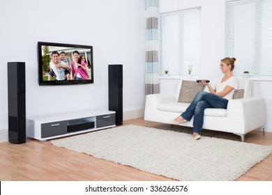 Full length of young woman watching television while sitting on sofa in living room