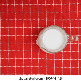 full Milk pitcher on red striped tablecloth background. top view. - Shutterstock ID 1909444429