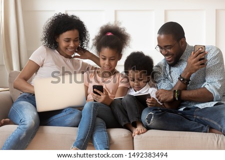 Full mixed-race family sit on couch having bad habit devices overuse addicted with electronic gadget laptop smartphone and tablet users spending lazy weekend at home, dependence of modern tech concept