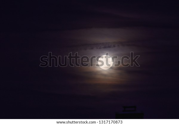 full moon behind veil\
clouds