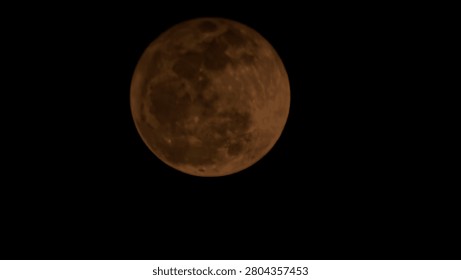 Full moon with a dramatic orange and copper hue glowing in a pitch-black night sky