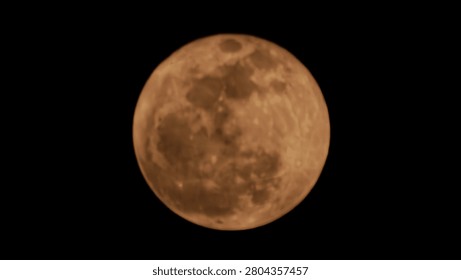 Full moon with a dramatic orange and copper hue glowing in a pitch-black night sky
