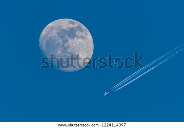 Full moon and\
flying plane with clear blue\
sky.