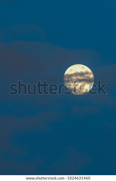 Full moon hiding behind the ripples clouds on the\
blue sky at dusk.