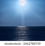 Full moon illuminating the clear, bluish night sky and with its rays of light beautifully reflected in the water of the Mediterranean Sea and illuminating a backlit fishing boat on the horizon line.