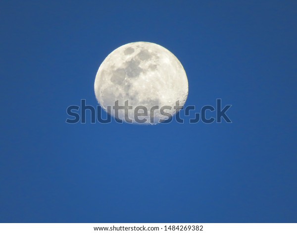 The full moon in a light blue\
sky. The brightness of the moon contrasts with the blue of the\
dusk.