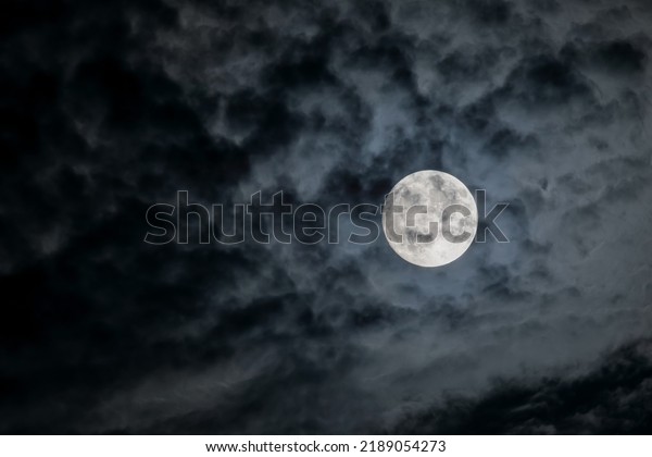 Full moon at\
night. The illuminated face of the moon is wrapped in a cloud cover\
that covers it in a veiled\
way.