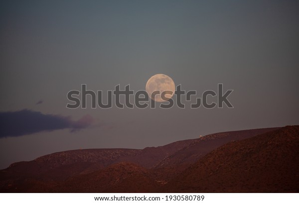 Full moon over barren landscape in Cabo de\
Gata red illuminated by sunset\
light