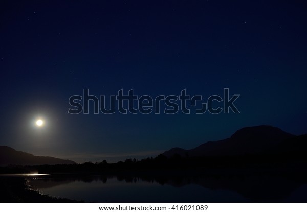 full moon reflection in river surface at night\
surrounded by stars and\
mountains