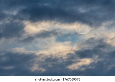 A Full Moon Is Rising Among The Clouds In A Day Time Sky