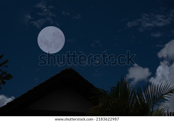 Full moon with roof house silhouette and clouds in\
the dark night.