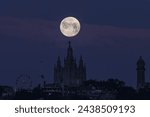 Full moon setting over the temple of the Sacred Heart of Jesus in Tibidabo,Barcelona.Next to the temple you can see an amusement park