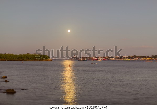 Full moon\
shine moonlight reflection in water at mactan strait cebu, people\
taking a bath in the sea and\
moonlight