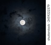 Full moon shining on cloudy Night sky background. Concept of Halloween, horror, mystic. Dramatic Dark spooky clouds around the moon. Earth satellite. Beauty in nature