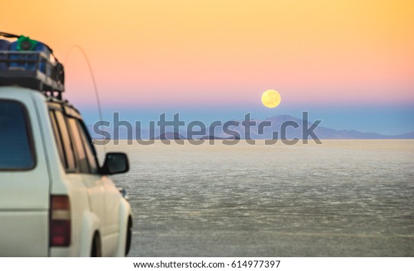 Full moon sunset with off road jeep vehicle on\
Salar De Uyuni - World famous nature wonder place in Bolivia -\
Travel and wanderlust concept in South American exclusive landscape\
- Focus on infinity