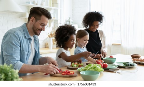 Full multinational family with cute daughters preparing dietary meal natural nutrition, cutting fresh vegetable for salad, parents caring for children health eat organic food, weekend activity at home