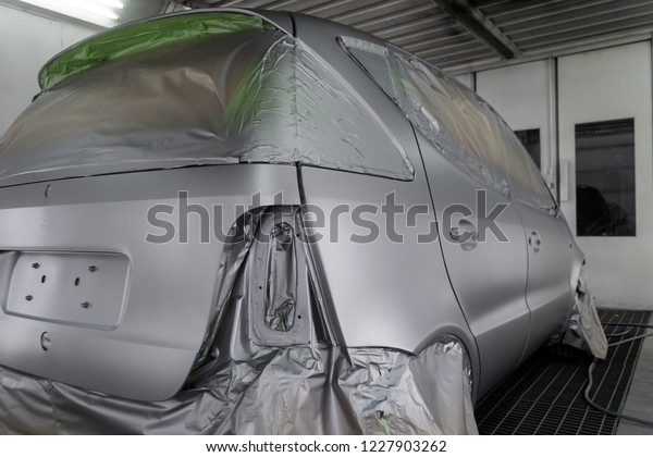 Full painting of a silver car in the body of a\
hatchback, some parts of which are protected by paper from splashes\
of paint droplets in a vehicle body repair workshop with a special\
box and equipment