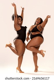 Full photo of superb plus size dark skinned two women in black fashionable swimwears, laughing and dancing, having fun together. Concept of body acceptance, body positivity and diversity.