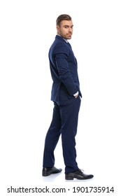 Full Picture Of Happy Young Guy In Navy Blue Suit Holding Hands In Pockets And Looking Over Shoulders, Standing Isolated On White Background In Studio