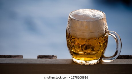 A Full Pint Of Foamy Lager Beer Stands On An Alpine Lodge Ledge.
