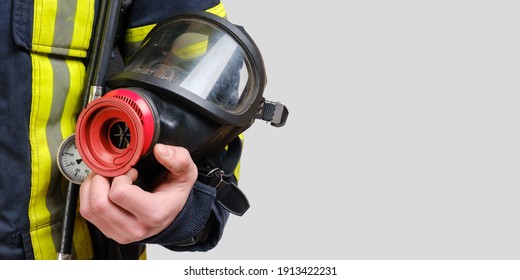 Full Protective Breathing Mask In Hand Of Unrecognized Firefighter, Rescue And Fire Fighter Equipment Isolated On Gray Background, Copy Space