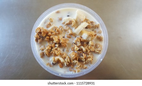 Full Of Protein And Multi Grains Clusters Or Granola With Lactose Free Skim Milk And Sliced Banana In Plastic Bowl On Stainless Table. Easy Healthy Breakfast Concept. Copy Space With Text. Top View.